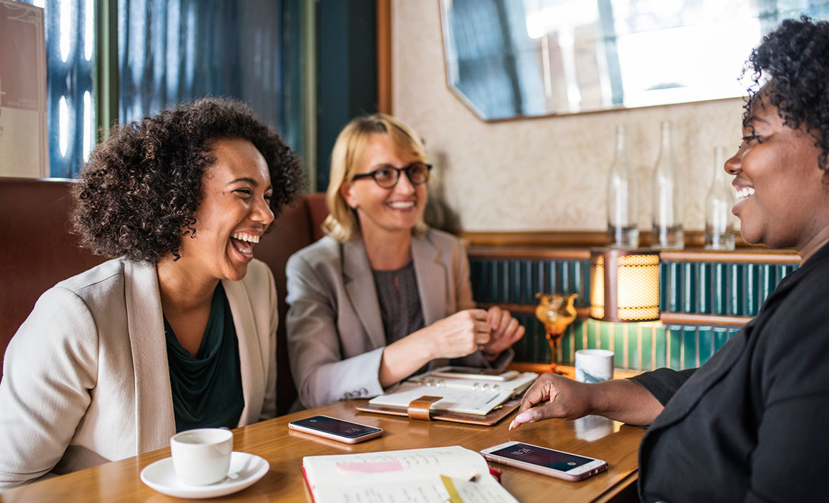 A group of young professionals laughing around a table, representing a dynamic and collaborative buyers agent team working together to assist clients.
