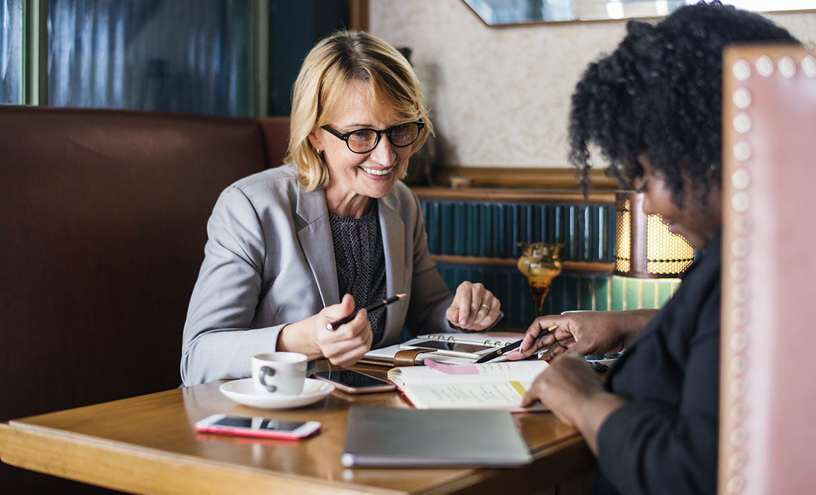 Two women discussing property details with paperwork on the table, representing the collaborative process of working with a buyers agent.