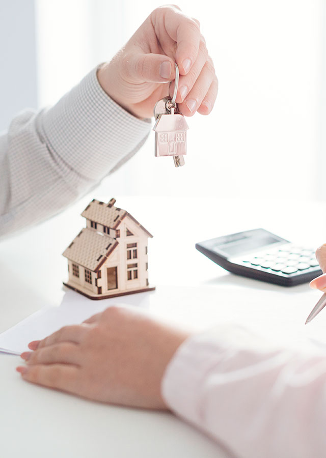 explaining what a buyers agent does, with a person handing over house keys and a wooden house prop in the background, symbolizing successful property purchase.
